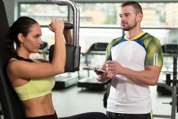 Mulher treina baú na máquina com personal trainer