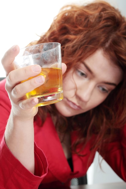 Mulher triste a beber uísque contra um fundo branco.