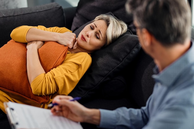 Foto mulher triste abraçando um travesseiro enquanto estava deitado no sofá do psiquiatra