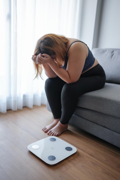 Mulher triste com gordura chateada com a dieta Perda de peso falha Dieta gorda e balança Mulher asiática triste na balança de peso em casa controle de peso