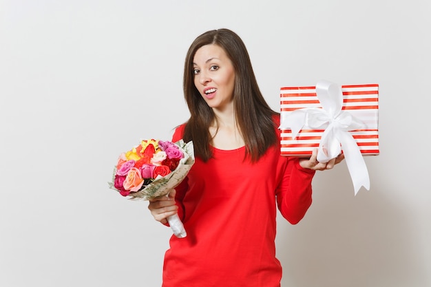 Mulher triste e chateada com roupas vermelhas, segurando um buquê de flores lindas rosas, caixa de presente com presente isolado no fundo branco. Dia de São Valentim, conceito de feriado de aniversário do dia internacional da mulher.