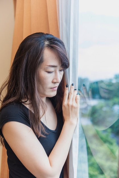 Mulher triste e deprimida em pé na janela