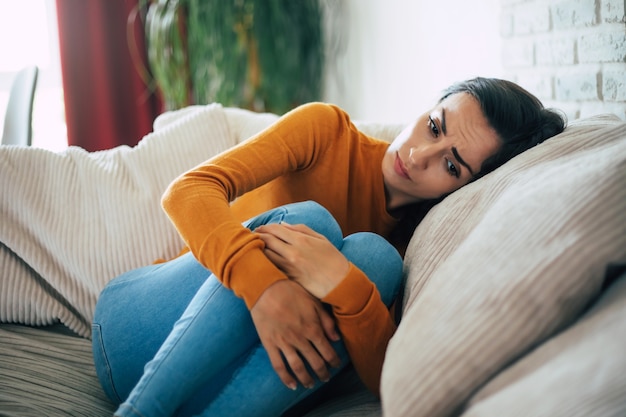 Mulher triste em profunda depressão está sentada no sofá, chorando e pensando na coisa ruim