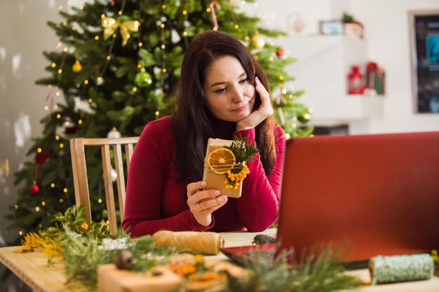 Mulher triste mostra a seus parentes como ela embala presentes para todos eles Mulher olhando em seu laptop árvore de Natal ao fundo