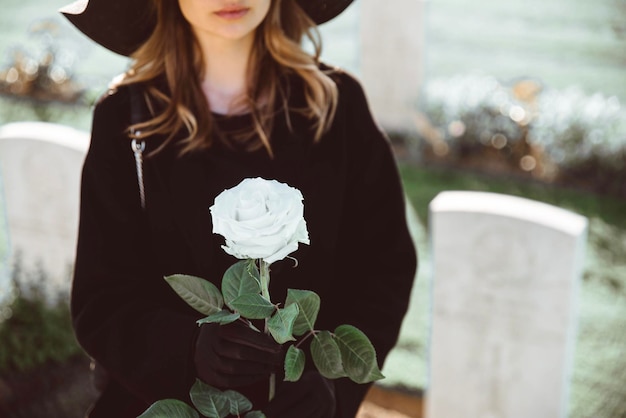 Foto mulher triste no cemitério segurando buquê de rosas na mão