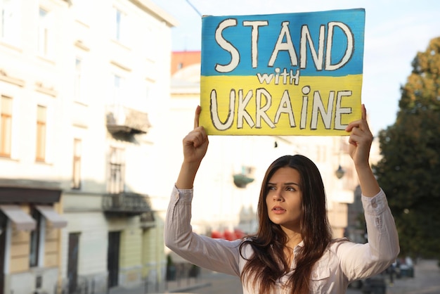 Mulher triste segurando cartaz nas cores da bandeira nacional e palavras Ficar com a Ucrânia na rua da cidade Espaço para texto