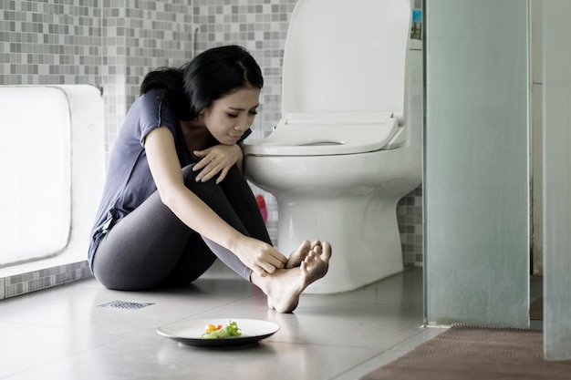 Mulher triste sentada com salada no banheiro