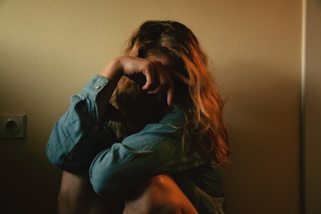 Mulher triste sentada contra a parede em casa