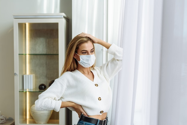 Mulher triste sozinha durante a pandemia de coronavírus usando máscara facial em casa para distanciamento social. Conceito de crise de saúde mental.