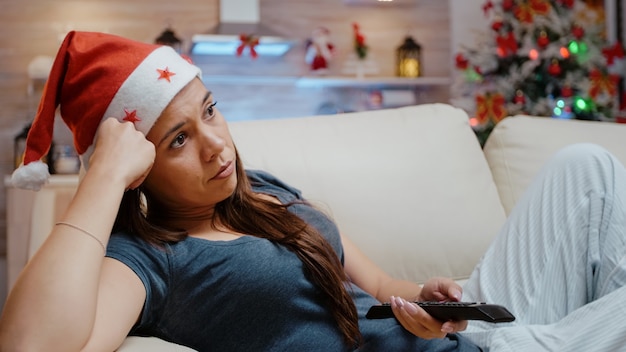 Mulher trocando de canal com o controle remoto da TV se sentindo entediada