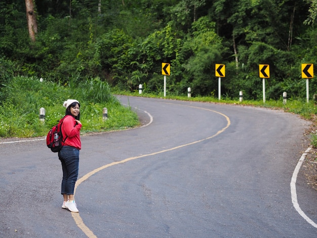 Foto mulher turista asiática caminhando na estrada sinuosa com sinal de alerta de curva na floresta. mochileiro moderno.