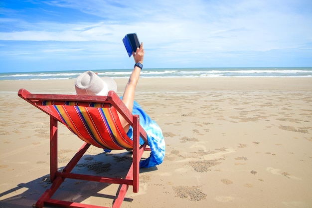 Mulher turista asiática descansando em uma espreguiçadeira à beira-mar segurando um smartphone para tirar uma selfie Apreciava as excursões marítimas durante as férias. Conceito de turismo natural na Tailândia