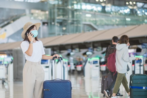 Mulher turista asiática usando máscara facial e usando smartphone móvel na proteção do aeroporto Infecção por doença de coronavírus Hora de viajar após o conceito de dose de reforço de vacina