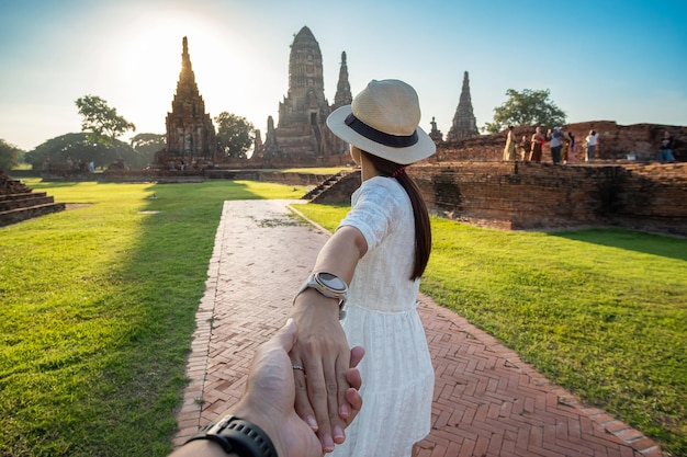 Mulher turista de vestido branco segurando o marido com a mão e caminhando para a antiga estupa no templo Wat Chaiwatthanaram no Parque Histórico de Ayutthaya, verão, juntos, siga-me, Ásia e Tailândia viajar