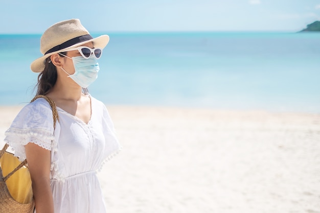 Mulher turista feliz usando máscara cirúrgica e curtindo o lindo mar e a areia branca