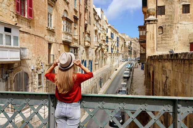 Mulher turista segura chapéu na ponte de ferro olhando a cidade velha de valletta malta