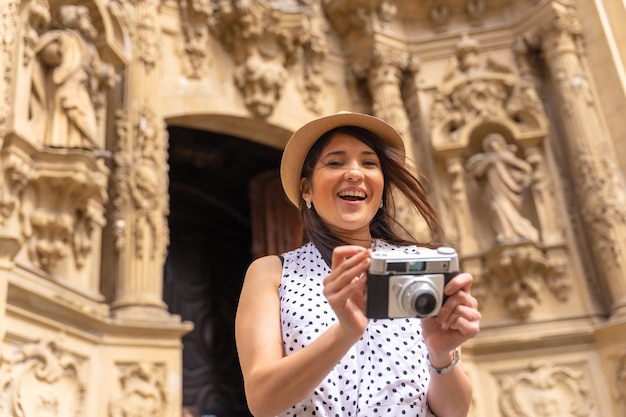 Mulher turista sorrindo com chapéu visitando uma igreja e tirando fotos com uma câmera aproveitando o conceito de férias de verão de viajante feminina e criadora de conteúdo digital