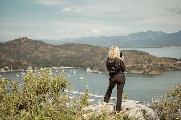 Mulher turista tendo vista smartphone sobre a baía e marina no mar Egeu viagens e caminhadas com aventura estilo de vida saudável ao ar livre mediterrâneo natureza nublado dia de primavera