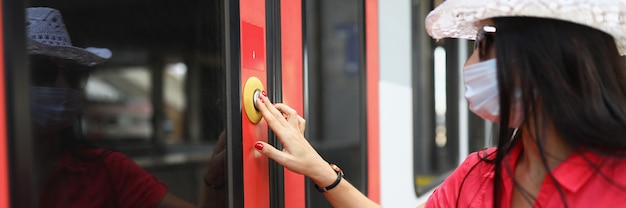 Mulher turista usando máscara protetora médica, pressionando o botão para abrir a porta do trem