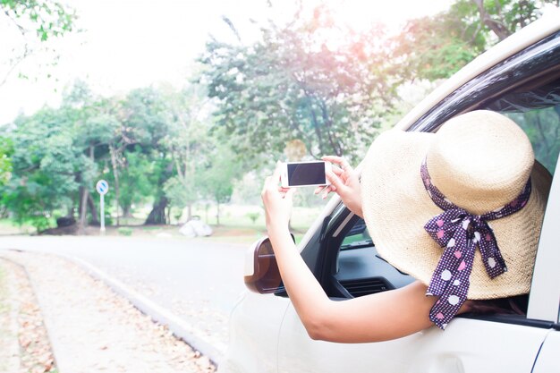 Mulher turística em chapéu usando smartphone tirando foto de seu carro, Viagem e vida feliz