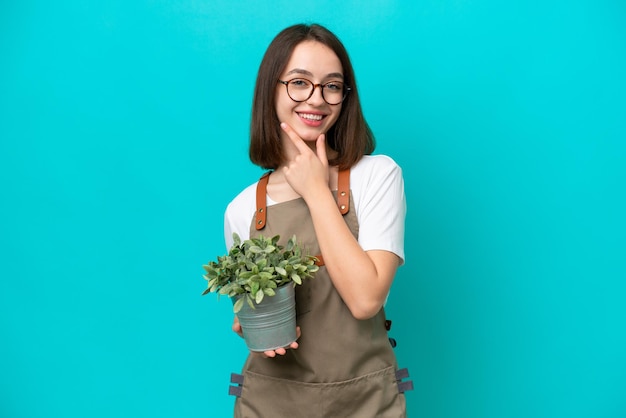 Mulher ucraniana de jardineiro segurando uma planta isolada em fundo azul feliz e sorridente