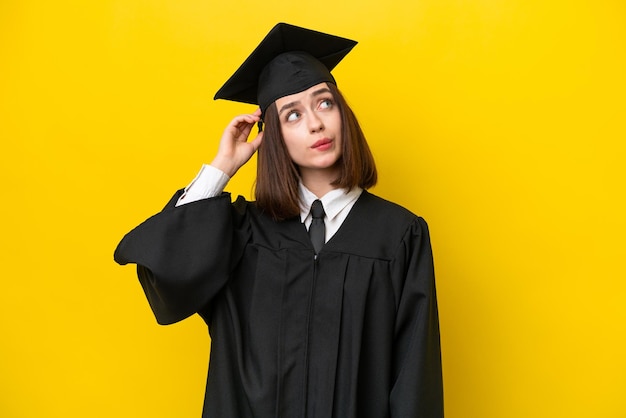 Mulher ucraniana jovem graduada na universidade isolada em fundo amarelo com dúvidas e com expressão facial confusa