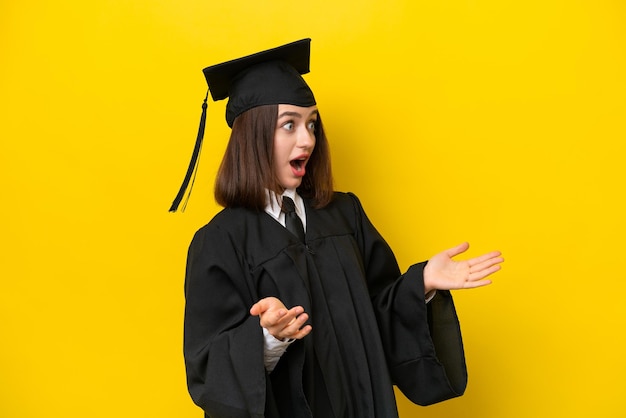 Mulher ucraniana jovem graduada na universidade isolada em fundo amarelo com expressão facial de surpresa