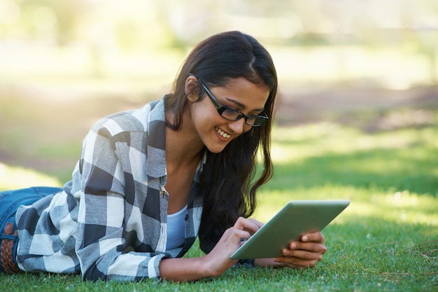 Mulher universitária e digitando em tablet no parque com projeto de pesquisa ou aprendendo ao ar livre no campus Estudante universitária e menina lendo on-line com educação de ebook e estudando na grama no jardim