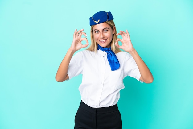 Mulher uruguaia aeromoça isolada em fundo azul, mostrando um sinal de ok com os dedos