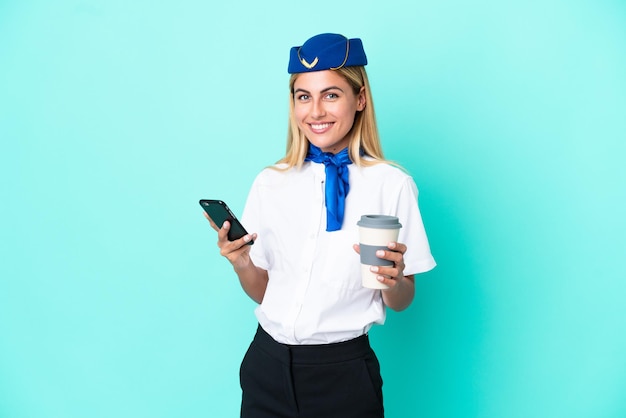 Mulher uruguaia com aeromoça isolada em um fundo azul segurando um café para levar e um celular