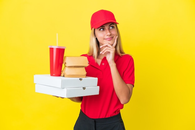 Mulher uruguaia de entrega segurando fast food isolada em fundo amarelo pensando em uma ideia enquanto olha para cima