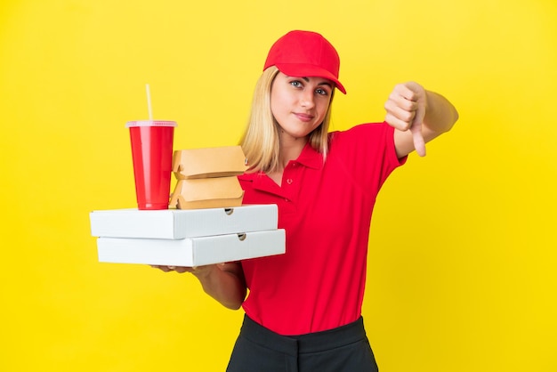 Foto mulher uruguaia de entrega segurando fast food isolado em fundo amarelo, mostrando o polegar para baixo com expressão negativa