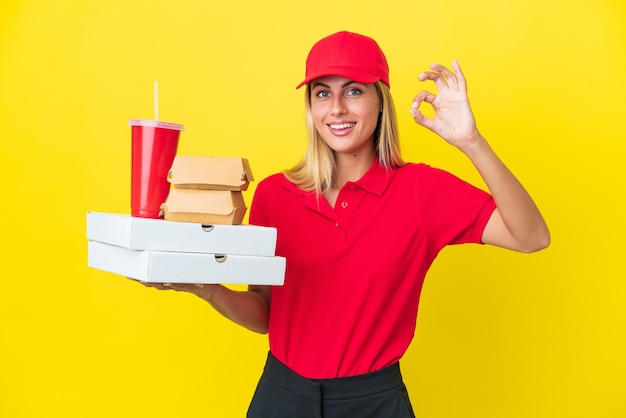 Mulher uruguaia de entrega segurando fast food isolado em fundo amarelo mostrando sinal de ok com os dedos