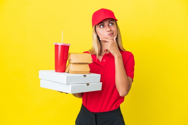 Mulher uruguaia de entrega segurando fast food isolado em fundo amarelo, tendo dúvidas