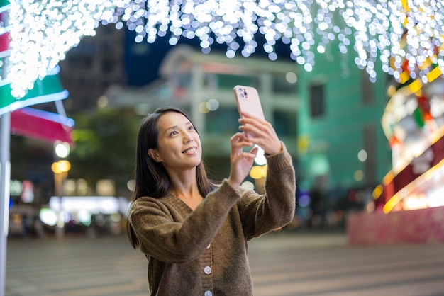 Mulher usa celular para tirar foto com o fundo da decoração de Natal da cidade