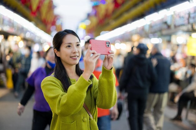 Mulher usa celular para tirar foto no mercado de rua em Taiwan