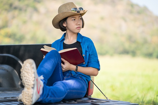 Mulher usa chapéu e lendo o livro na caminhonete