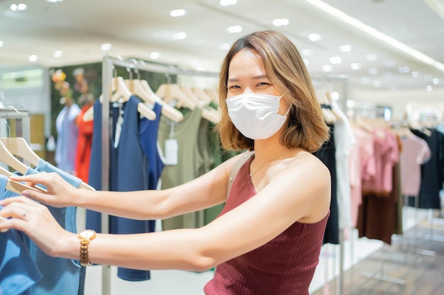 mulher usa máscara facial e escolhe vestido na loja de moda em loja de departamentos