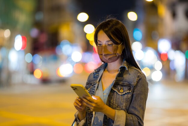 Mulher usa máscara facial e usa celular à noite