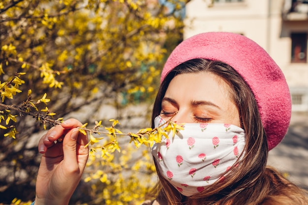 Mulher usa máscara reutilizável ao ar livre durante a pandemia de coronavírus covid-19. mulher cheira flores. fique seguro