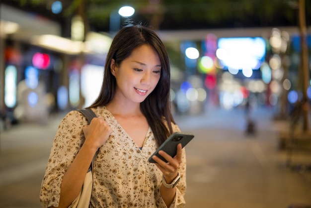 Mulher usa telefone celular na cidade à noite