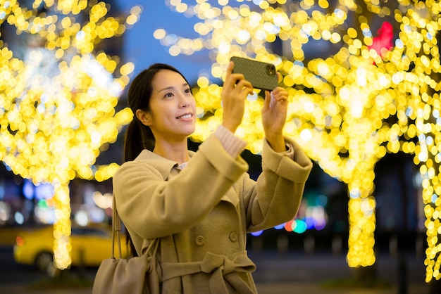 Mulher usa telefone celular para tirar foto na cidade à noite