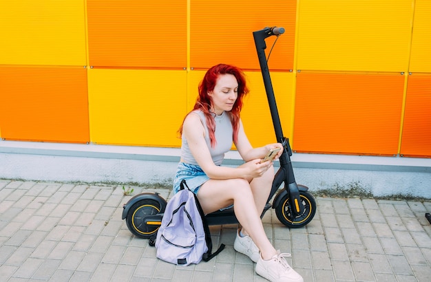 Mulher usa um smartphone e uma scooter elétrica no verão na cidade