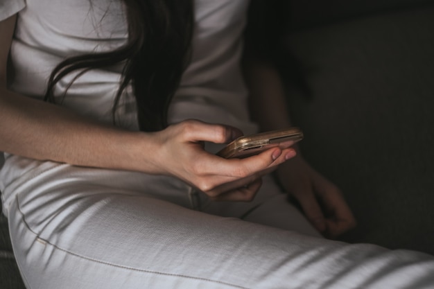 Mulher usa um smartphone enquanto está sentada em casa em um sofá à noite