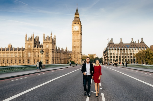 Mulher usa vestido elegante vermelho e homem de mãos dadas, passear na ponte de westminster, admirar as vistas de londres