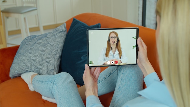 Foto mulher usando aplicativo médico em tablet digital, consultando um médico por meio de videoconferência