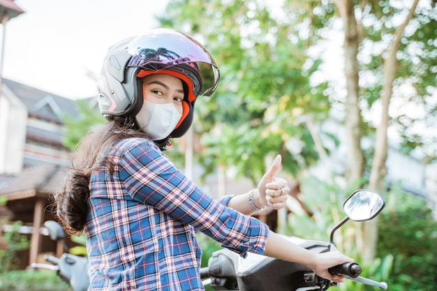 Mulher usando capacete e máscara com polegares para cima enquanto andava de moto na estrada