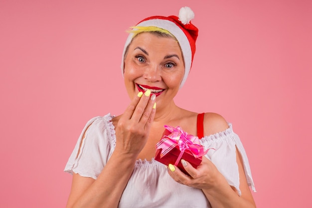 Mulher usando chapéu de Papai Noel vermelho e segurando a caixa de presente no fundo rosa do estúdio.