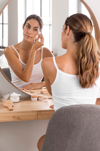 Mulher usando creme e olhando no espelho conceito de autocuidado