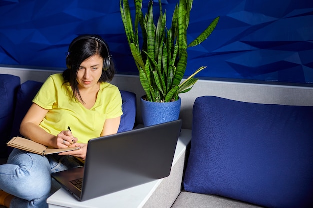 Mulher usando fones de ouvido, estudando online usando um notebook